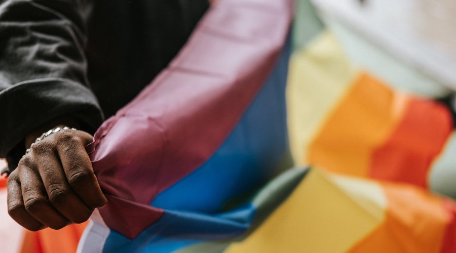 Crop faceless African American homosexual male in casual clothes showing colorful rainbow flag on street