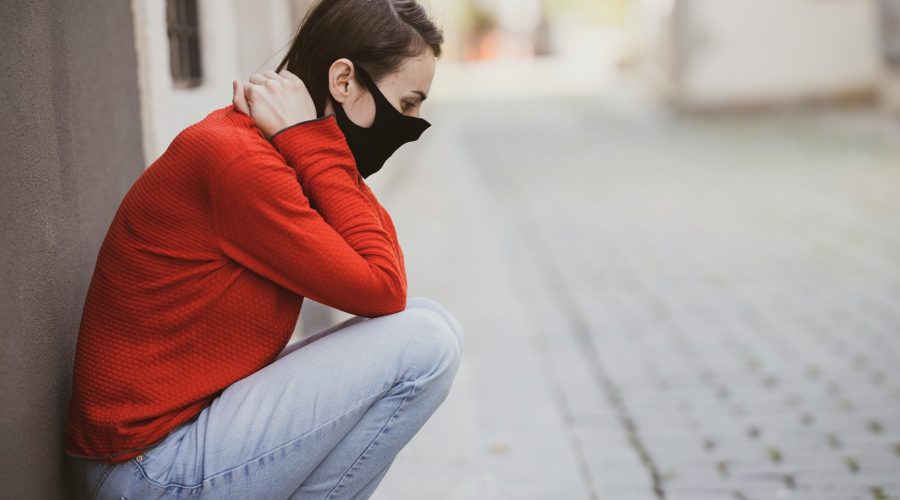 woman in red sweater and blue denim jeans sitting on concrete pavement