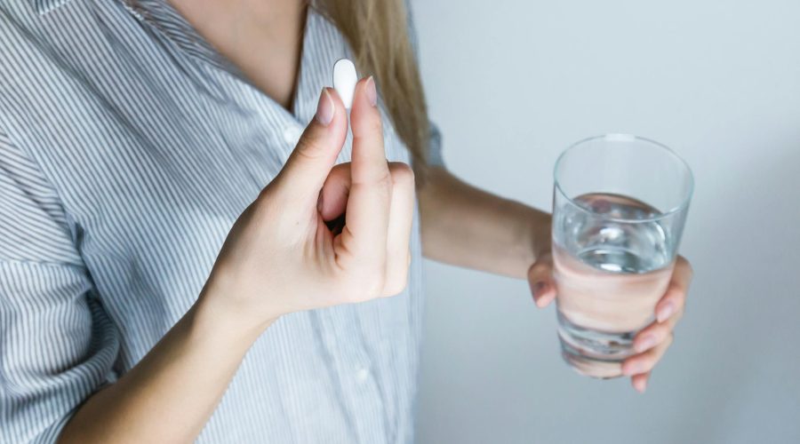 Woman Holding Half-full Glass and White Medicine Pill
