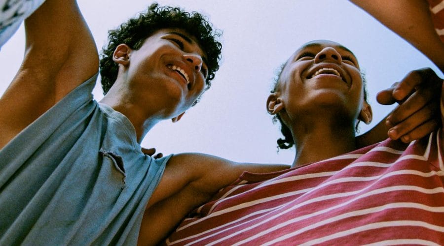 Happy group of teenagers enjoying a moment together under blue sky, symbolizing friendship and fun.
