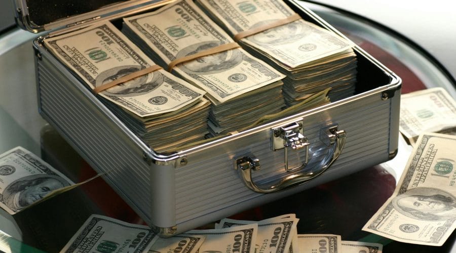 Open briefcase filled with stacks of hundred dollar bills on a glass table, representing wealth.