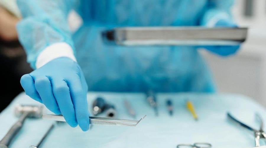 Blue-gloved hand handles surgical tools in a medical setting, focusing on precision and cleanliness.
