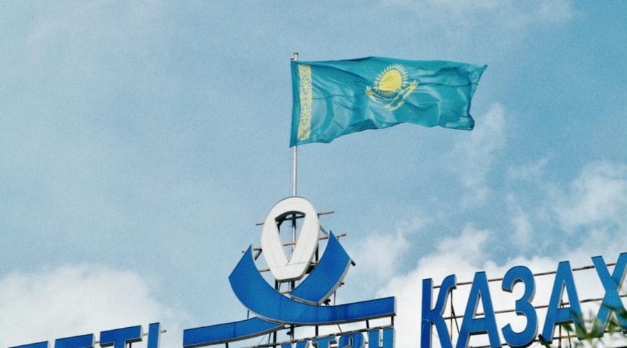 Kazakhstan national flag waving atop a modern building in Almaty under a clear blue sky.