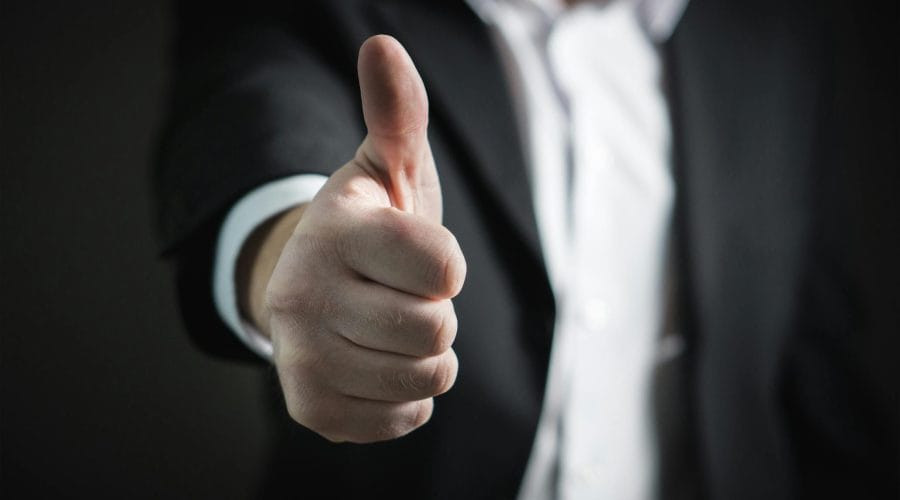 A close-up of a man's thumbs up gesture, symbolizing success and agreement.